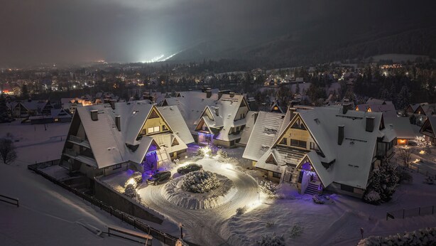 Ein verschneites Dorf mit traditionellen Chalets, einer zentralen, kreisförmigen Auffahrt und einem Berg im Hintergrund.