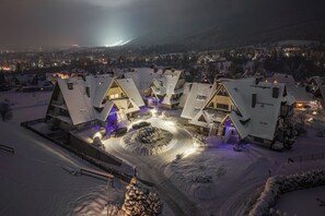 Un pueblo cubierto de nieve con edificios de estilo chalete tradicional, un camino circular central y un telón de fondo montañoso.