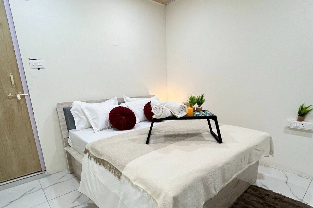 A neatly arranged bedroom with a bed, pillows, a bedside table with a lamp, and a small plant.