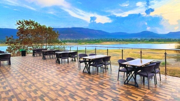 An outdoor dining area with tables and chairs, a wooden floor, and a view of a lake and mountains. - Sizzle Bay Resort (Mawal)