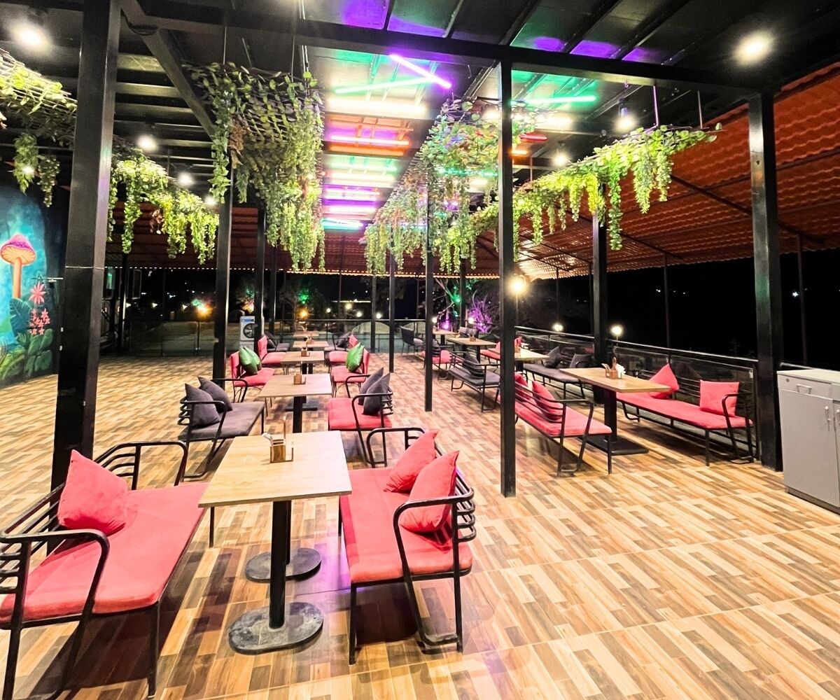 An indoor dining area with wooden flooring, red cushioned seating, and hanging plants.