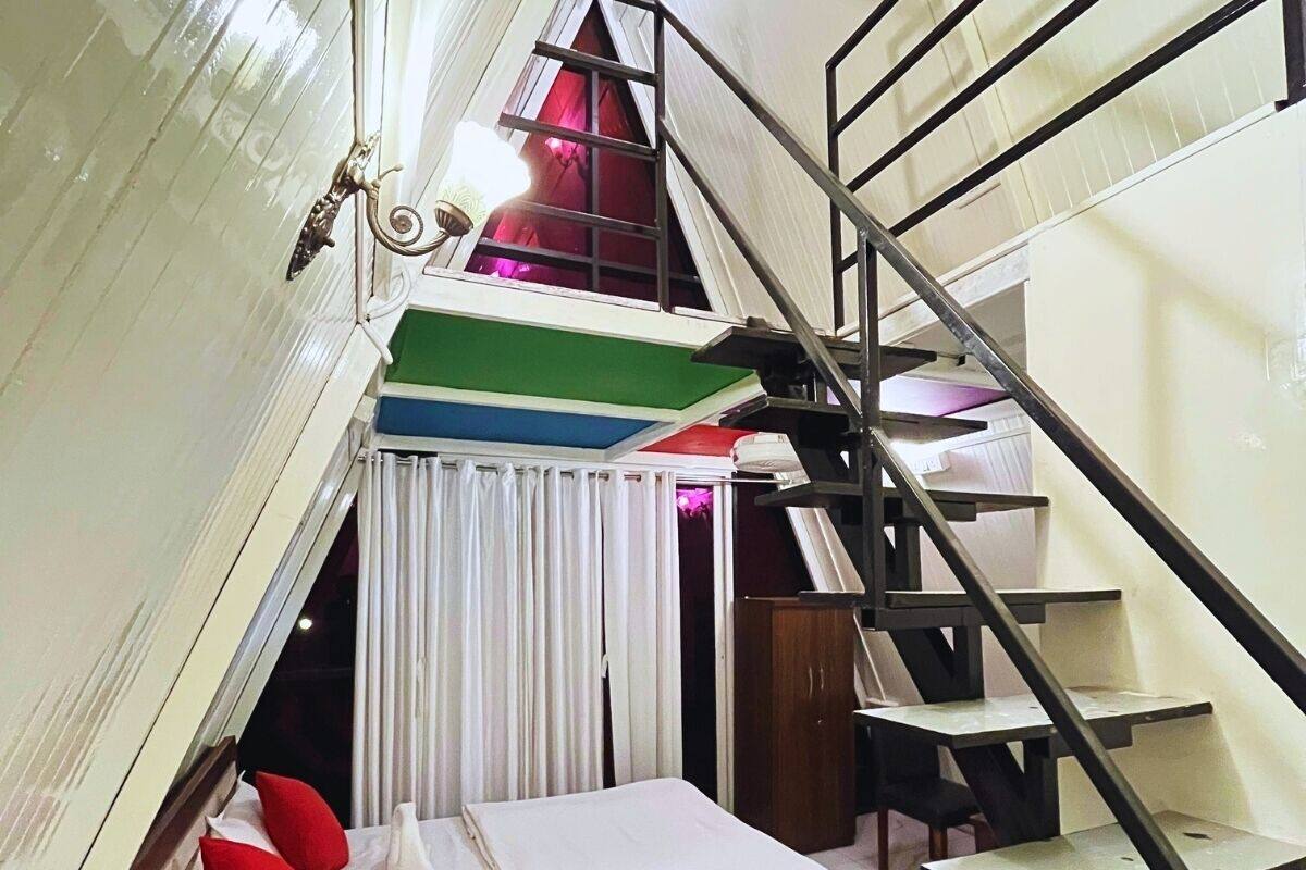 A dorm-style room with a bunk bed, a staircase, and a window with curtains.