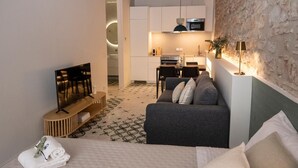 A modern hotel room with a grey sofa, a TV, a bed, and a kitchen area in the background. - Montgo Loft Apartment (Dénia)