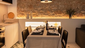 A modern kitchen with a stone wall backsplash, a dining area with a table set for two, and a view of the sea through a window. - Montgo Loft Apartment (Dénia)