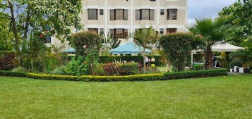Un hotel con un jardín cuidado, mobiliario de exterior y un edificio de varios pisos con balcones.