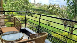 A balcony with wicker furniture and a glass table, overlooking a well-maintained garden and distant buildings. - Royal Green Gardens (Nakuru)
