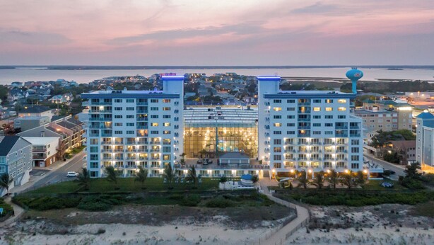 Un grand hôtel à plusieurs étages, avec une plage au premier plan et une vue sur la mer en arrière-plan.