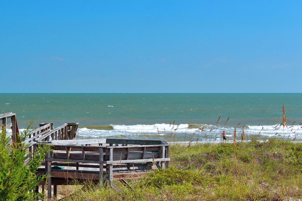 A wooden pier extending into the ocean with a person walking on it.