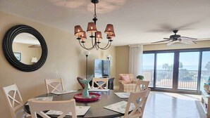 Un coin repas avec une table ronde, des chaises blanches, un lustre et une vue sur la mer grâce à de grandes fenêtres.