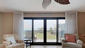 Un salon avec deux canapés, une table basse et une vue sur un balcon donnant sur un espace verdoyant et des bâtiments en arrière-plan.