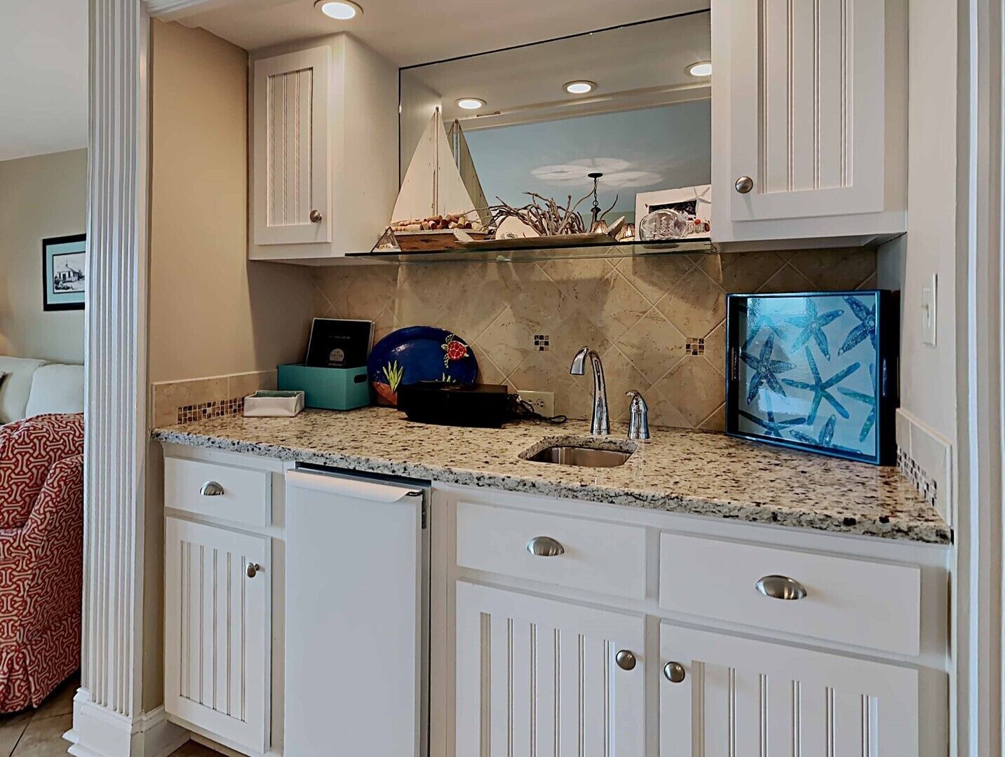 A kitchen with white cabinetry, a granite countertop, a sink, and a decorative mirror above the countertop.