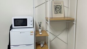 A compact kitchenette with a microwave, a small fridge, and a shelf unit with a framed picture and a vase. - SRR STAY (Gwangmyeong)