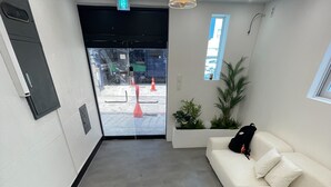 A reception area with a white sofa, a hanging pendant light, and a potted plant. - SRR STAY (Gwangmyeong)