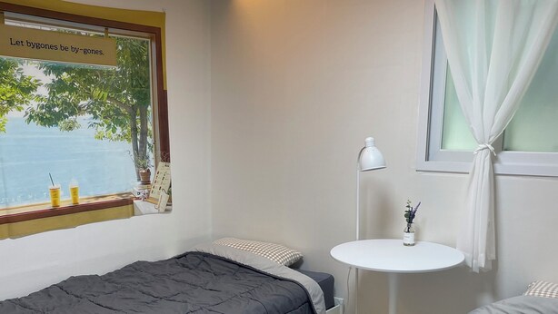 A bedroom with two beds, a small white table, a window with a view, and a sign on the window. - SRR STAY (Gwangmyeong)