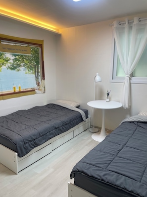 A bedroom with two beds, a small white table, a window with a view, and a sign on the window. - SRR STAY (Gwangmyeong)