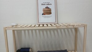 A wooden shelf unit with a framed picture of pancakes, a hairdryer, and a folded towel. - SRR STAY (Gwangmyeong)