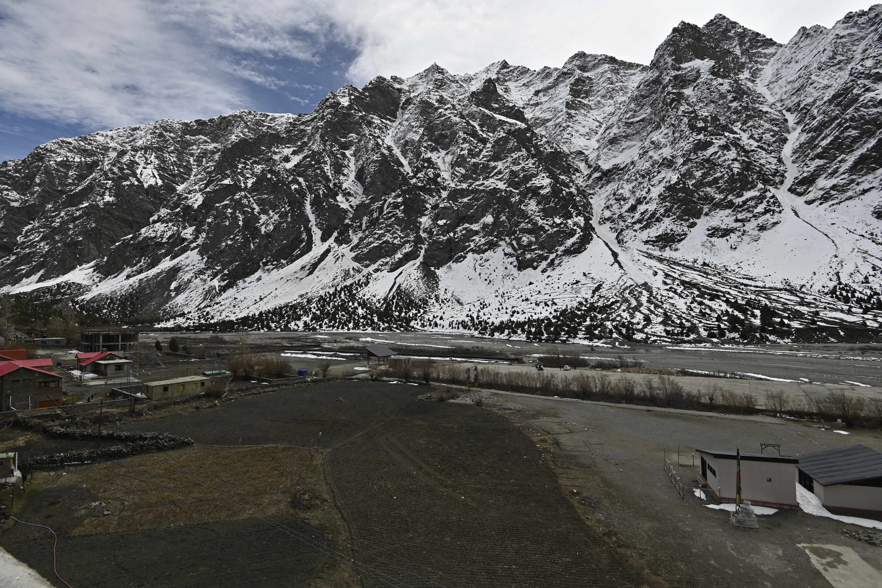 Paisagem montanhosa com picos cobertos de neve, área pavimentada com edifícios e céu claro.