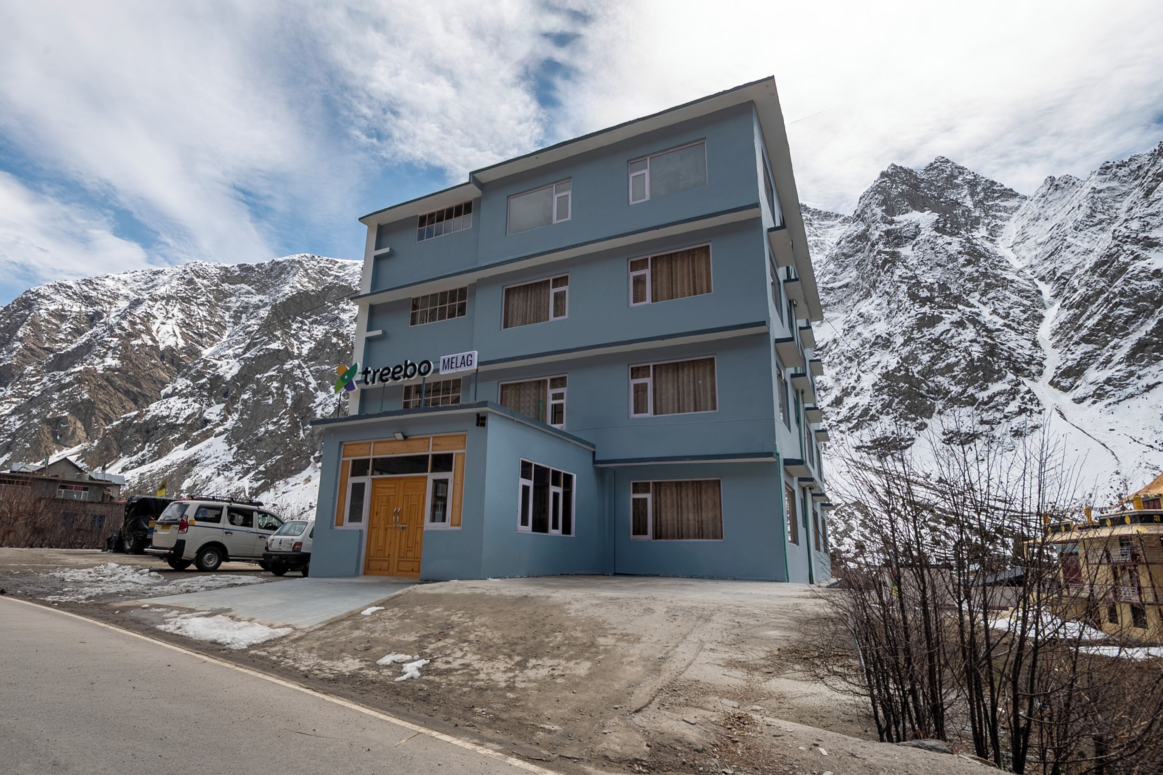 Un hotel de varios pisos con un letrero que dice 'treebo MELAG' al frente de un paisaje montañoso.