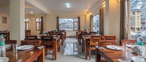 A hotel dining area with multiple tables, chairs, and large windows offering a view of a snowy landscape.