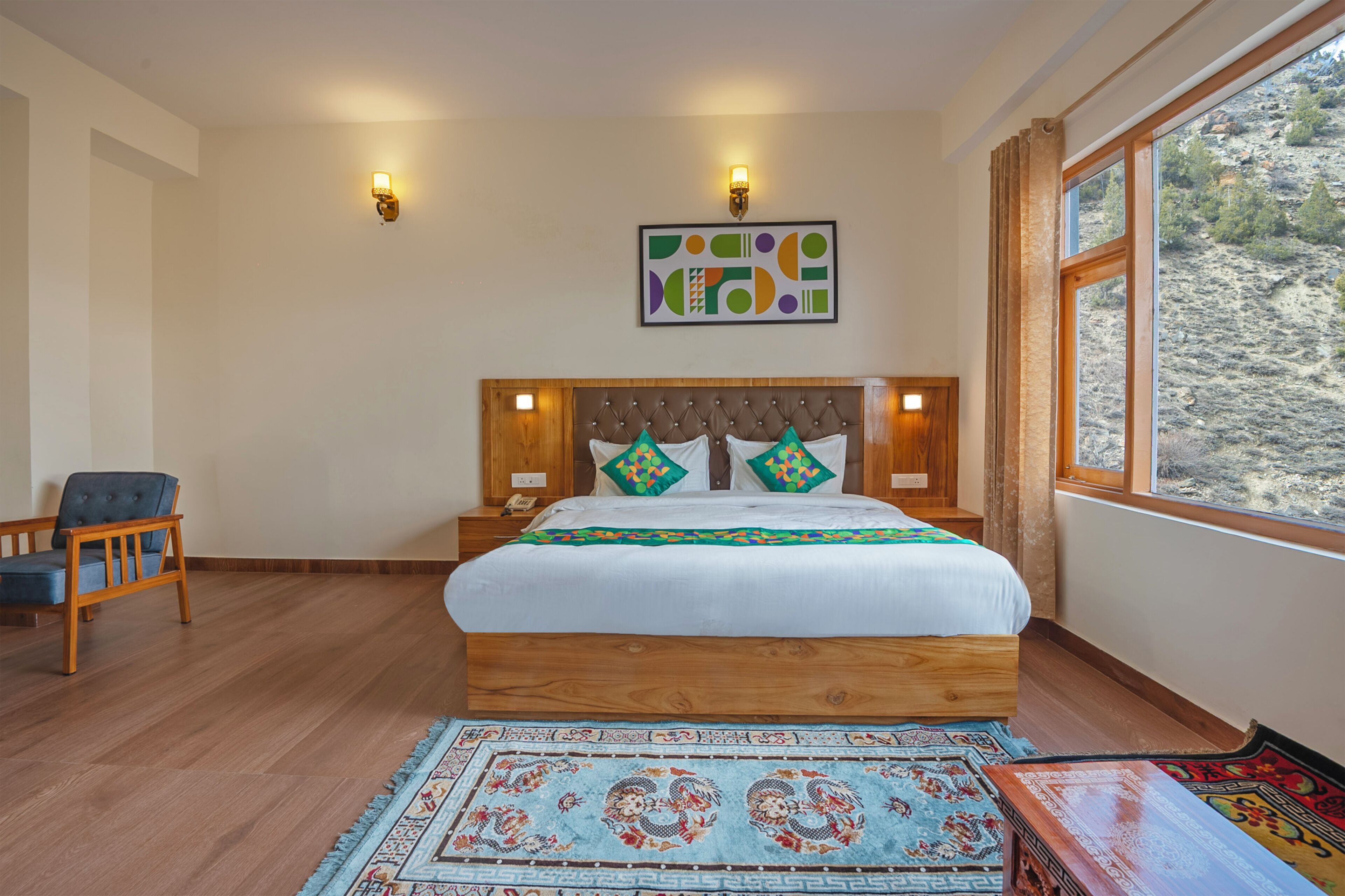 Un dormitorio con una cama de madera, dos lámparas de noche, una silla, una alfombra y una ventana con vistas a la montaña.
