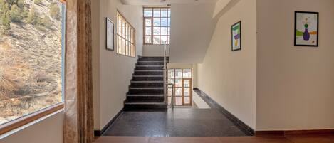 A staircase leading to an upper floor, with a view of a mountainous landscape through a window.