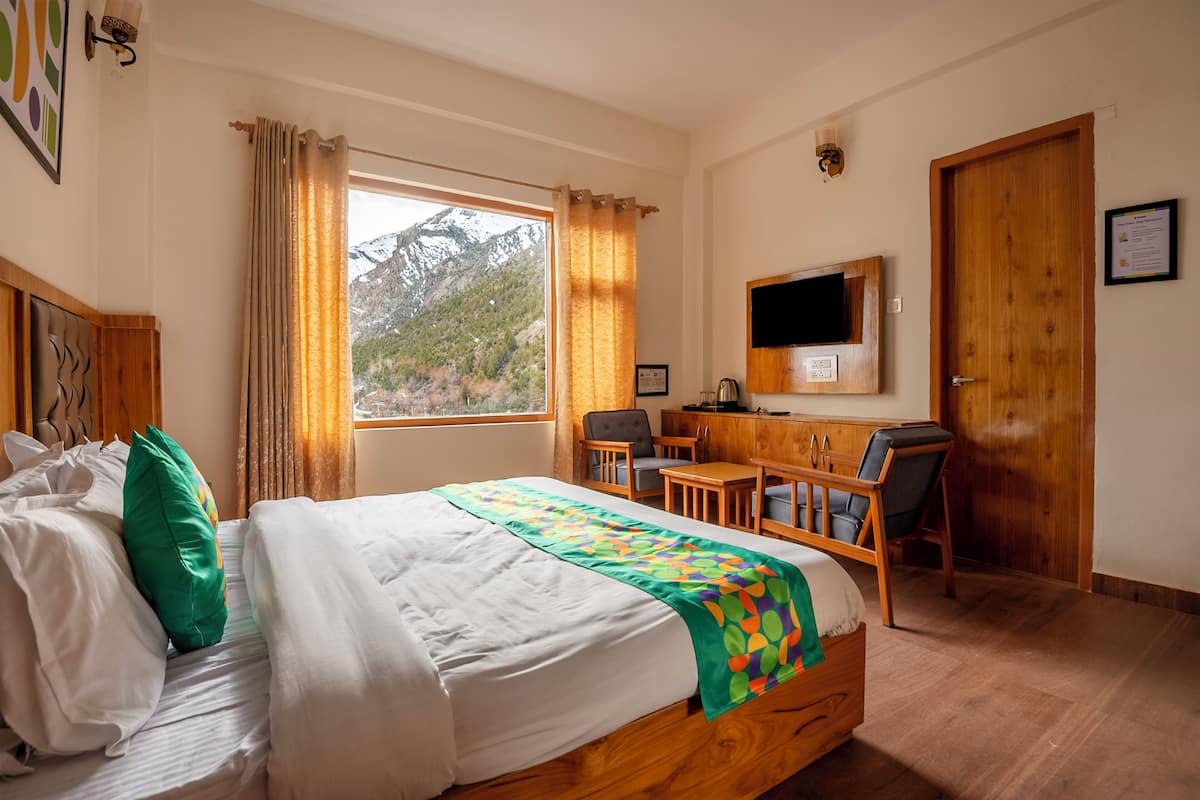 A bedroom with a bed, a desk, a chair, a TV, and a window with a mountain view.