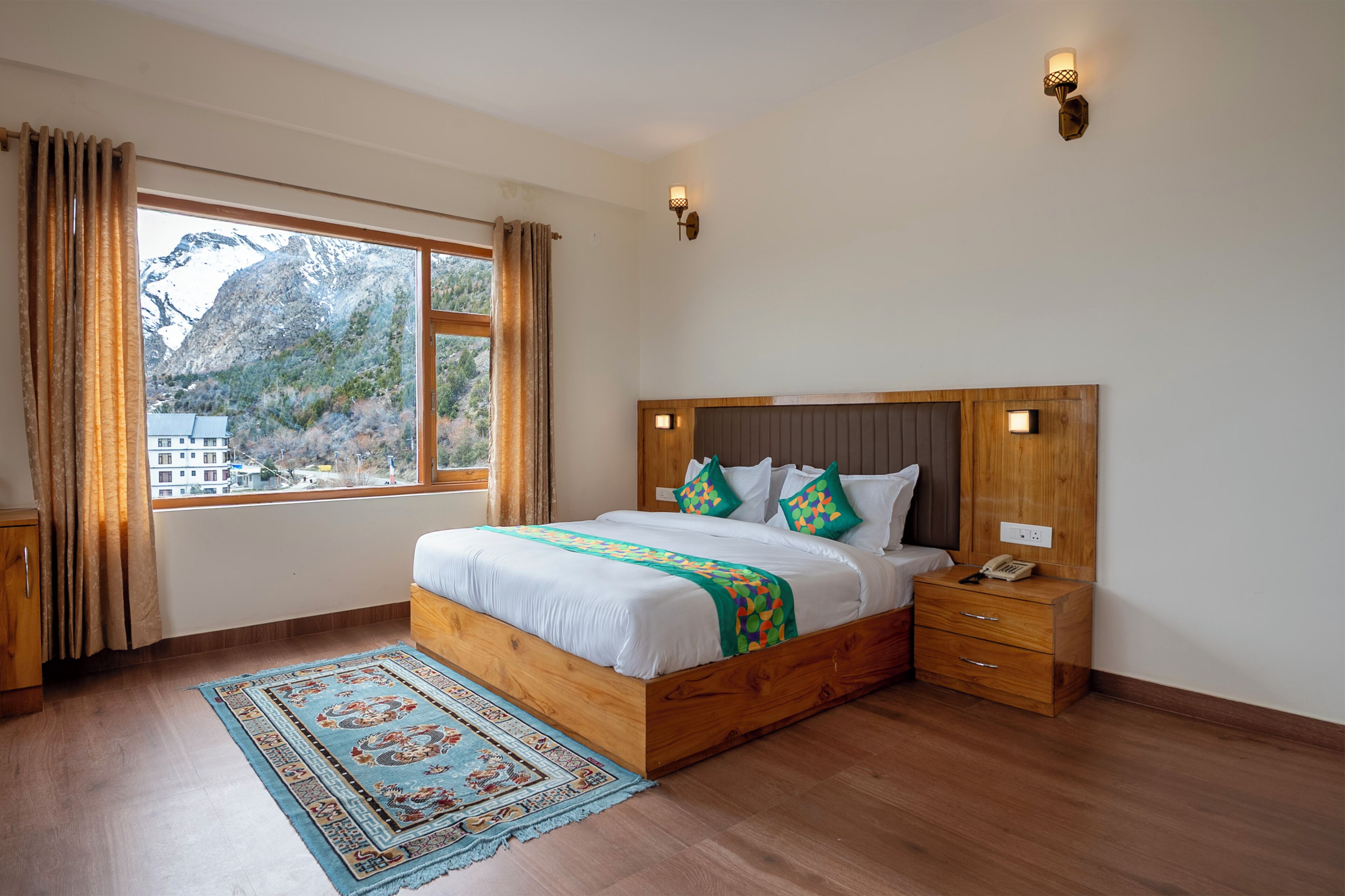 A bedroom with a wooden bed, a nightstand, a telephone, and a view of mountains through a window.