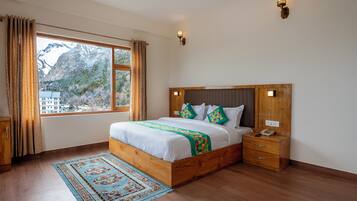 A bedroom with a wooden bed, a nightstand, a telephone, and a view of mountains through a window.