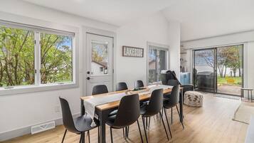 A modern dining area with a wooden table, black chairs, and a view of a backyard through large windows.