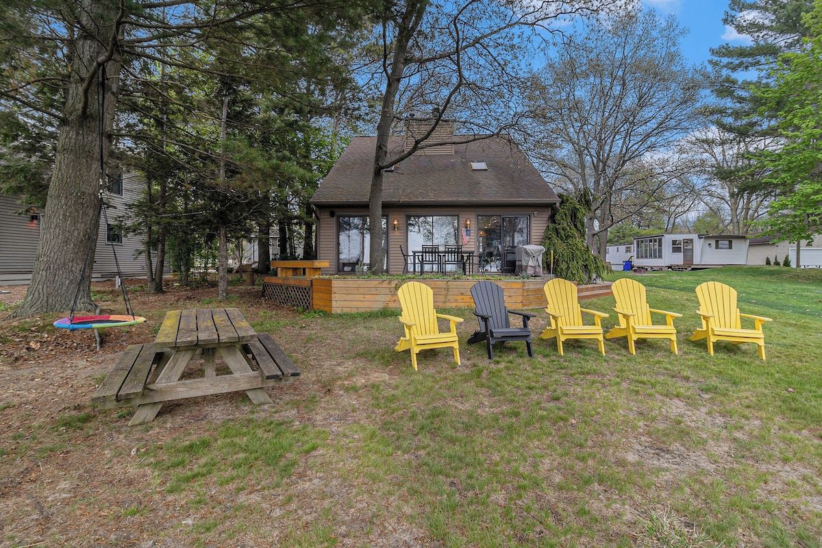A backyard with a wooden picnic table and four Adirondack chairs.