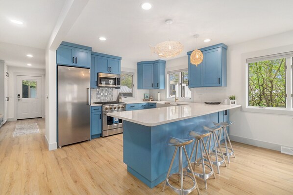 A modern kitchen with blue cabinets, stainless steel appliances, and a large island with bar stools.
