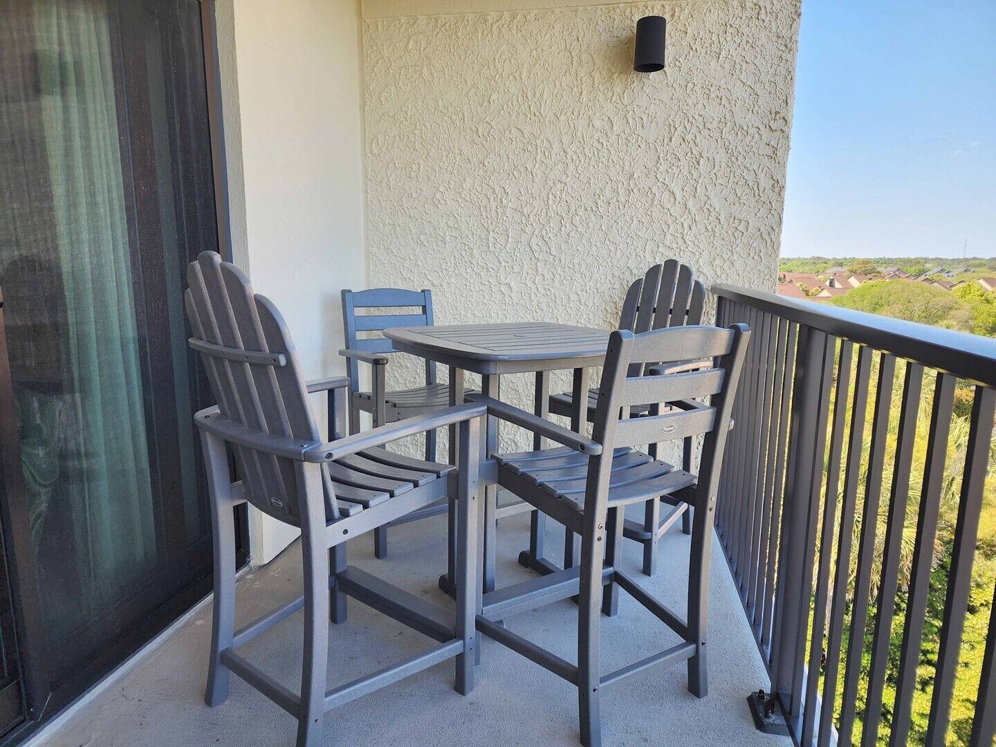 A balcony with a table and chairs, a textured wall, and a railing.