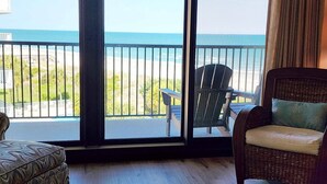 A room with a view of the beach, a wicker chair, a patterned ottoman, and a large window.