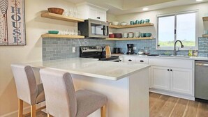 A modern kitchen with a central island, bar stools, a microwave, and a sink.