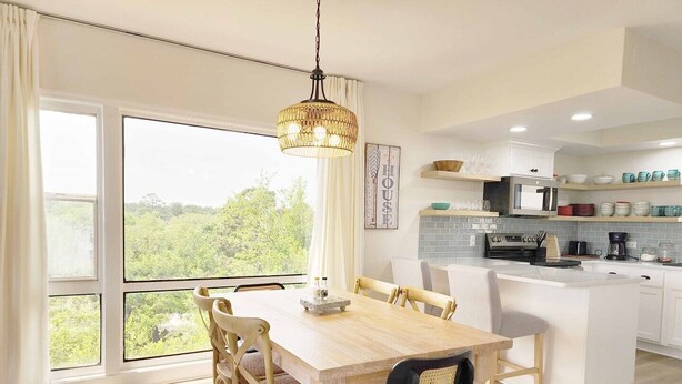 A modern kitchen with a central island, large windows, and a dining area with wooden chairs.
