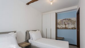 A bedroom with two beds, a wardrobe, a nightstand, and a wall painting. - Appartamento Centrale con Terrazzo by Wonderful Italy (Santa Margherita Ligure)