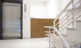 Un ascensor moderno, un revestimiento de pared de madera y una escalera blanca.