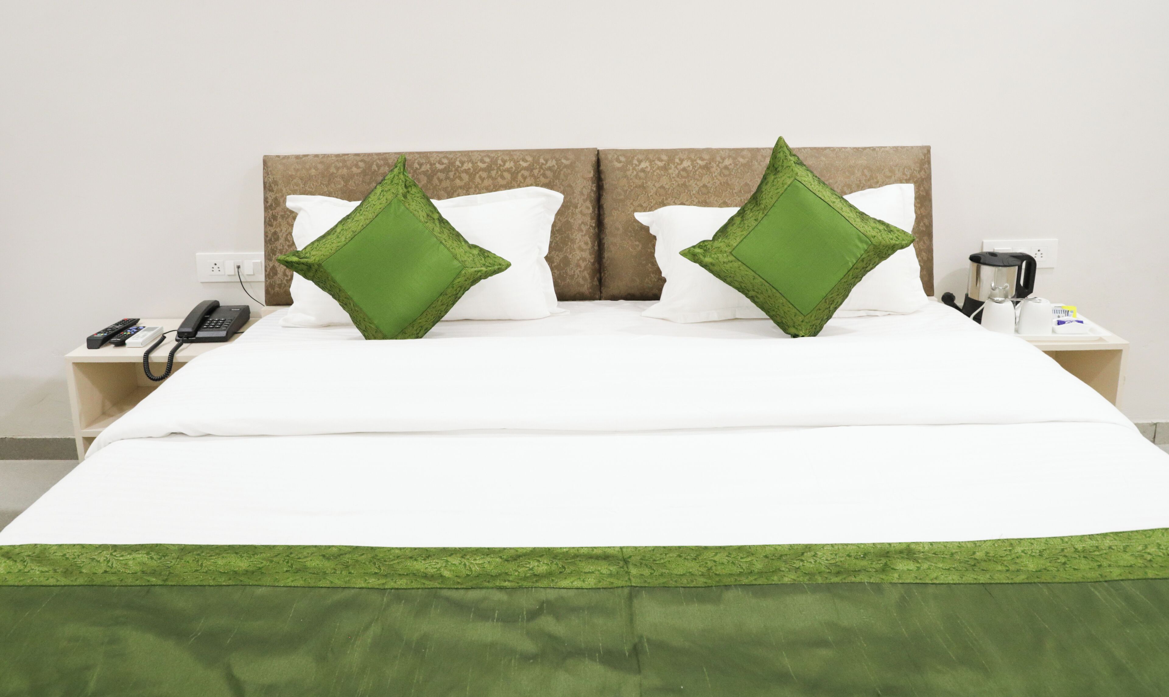 A neatly made bed with white and green bedding, a telephone, and a coffee maker on a bedside table.