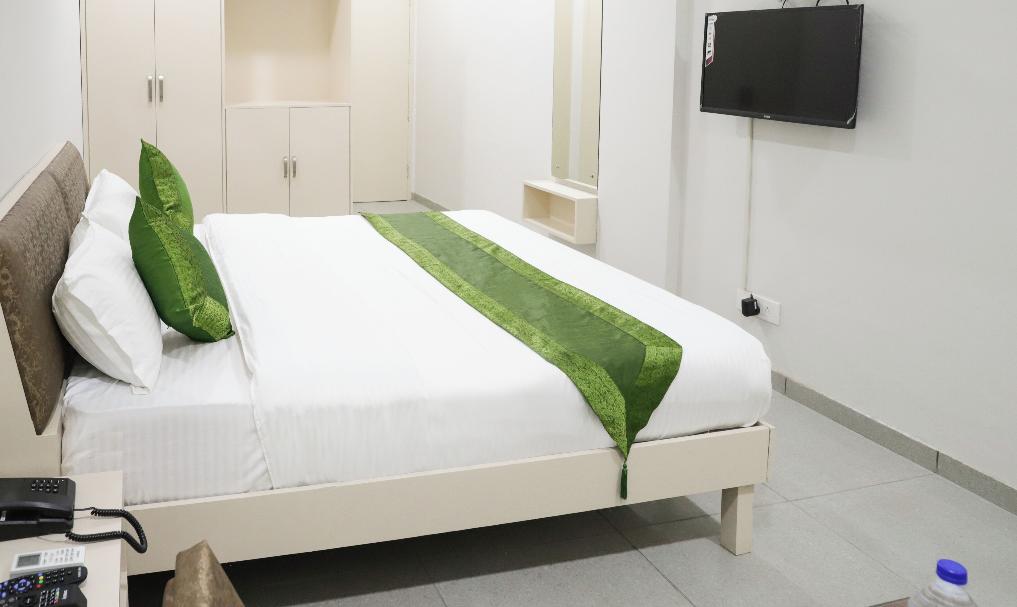 Ein ordentlich bezogenes Bett mit weißer und grüner Bettwäsche, ein Nachttischtelefon und ein an der Wand montierter Fernseher.