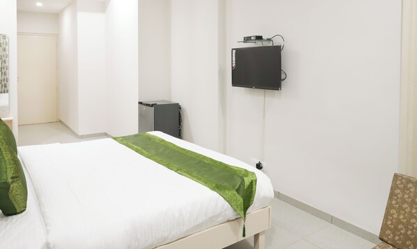 Un dormitorio con una cama, un televisor en la pared y un armario pequeño.