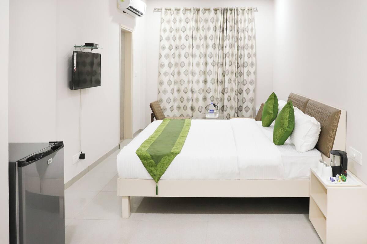 A neatly made bed with a green throw, a bedside table with a bottle, and a TV mounted on the wall.