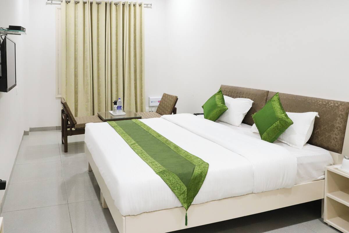A neatly made bed with white and green linens, a wooden headboard, and a bedside table with a water bottle and a cup.