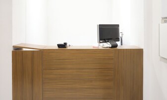 Un mostrador de recepción de madera con un monitor de pantalla plana, un teléfono y una pequeña caja blanca.