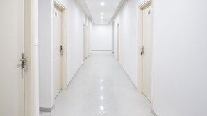 A long, narrow hallway with white walls and doors, leading to a bright, well-lit room.