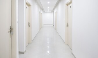 Un pasillo largo y estrecho con paredes y puertas blancas que conduce a una habitación luminosa y bien iluminada.