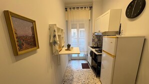 A narrow kitchen with a refrigerator, a coffee maker, and a clock on the wall.