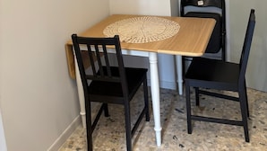 A small dining area with a wooden table, two black chairs, and a white wall.