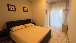 A hotel room with a large bed, a nightstand, a wall-mounted air conditioner, and a door leading to a balcony with a view.