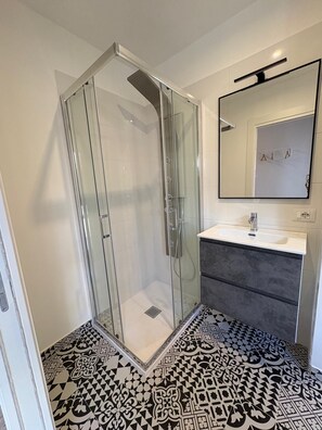 Un baño con ducha de vidrio, un lavamanos blanco y un mueble de tocador de tonos oscuros.