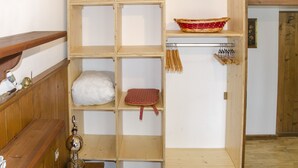 A room with wooden shelves, a white pillow, a red patterned bag, a basket, and a wall-mounted drying rack. - Casa Salvaniera (San Vito di Cadore)